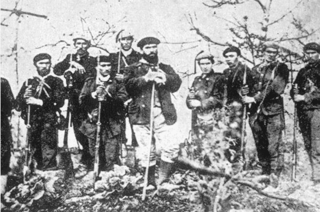 Armed soldiers standing in a rural landscape during the Third Carlist War, holding rifles and posing together in a wartime setting.
