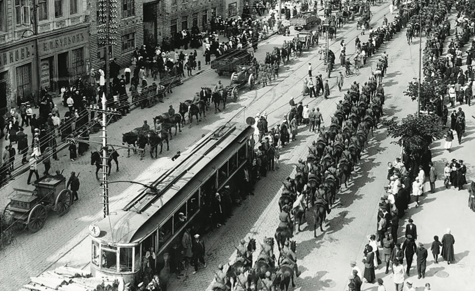 Busy Russian city street with a crowded tram and a long column of cavalry soldiers on horseback parading through civilians.