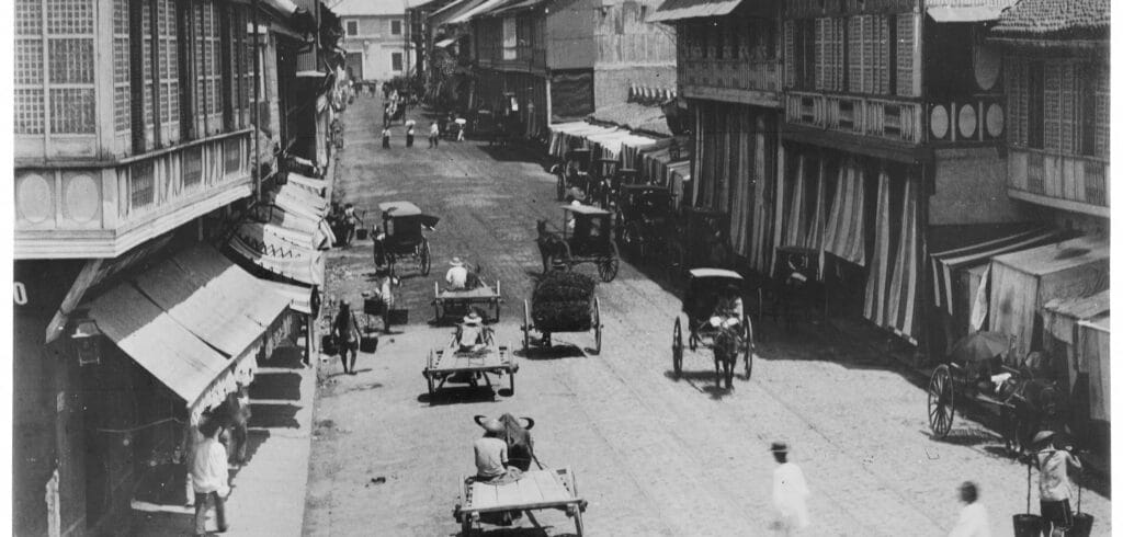 Busy street scene in Manila around 1900 with horse-drawn carts, colonial houses, and everyday urban life under Spanish rule